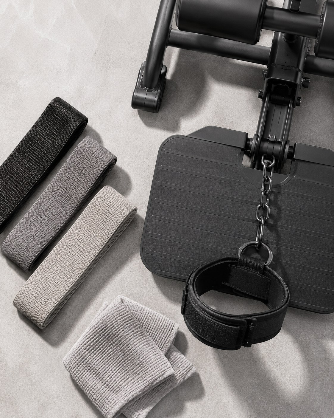 Flat lay of resistance bands and an ankle cuff beside a cable glute kickback machine platform